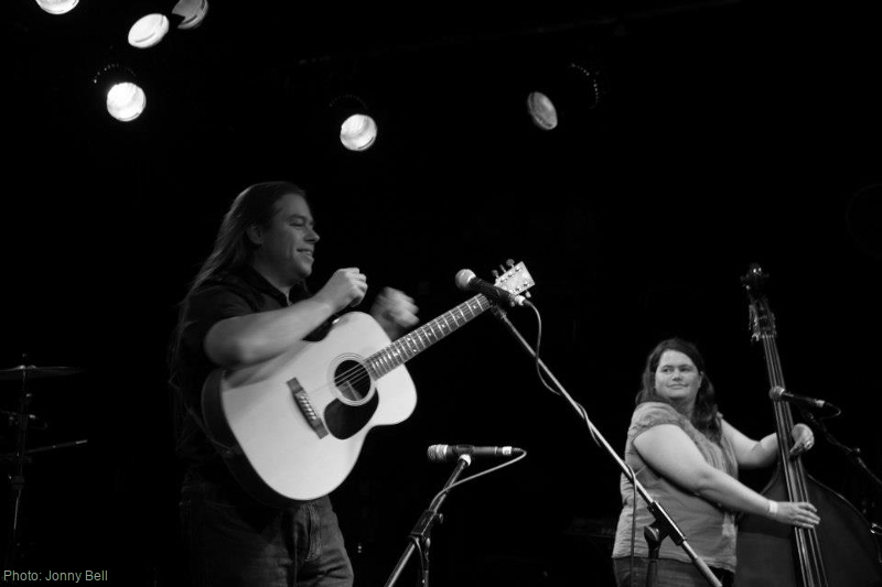 Photograph of David Rozzell wearing a OOO-18 acoustic guitar, stood next to Clare Rozzell with a double bass, on stage at The Wedgewood Rooms, Portsmouth.